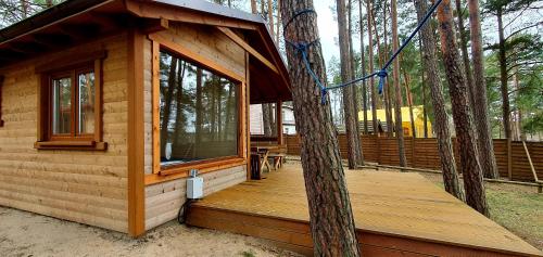 a log cabin with a deck in the woods at Domki Borsk - nad samym jeziorem, nowe w pełni wyposażone z miejscem parkingowym in Borsk