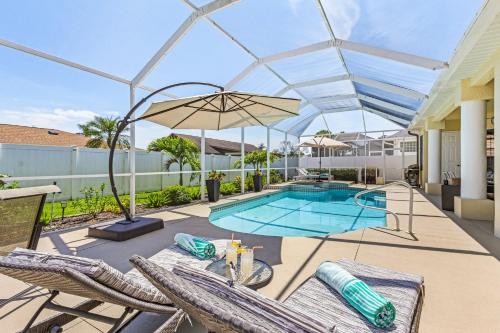 a pool with chairs and an umbrella on a patio at Villa Haze, Private Heated Pool & Spa, South Cape Coral in Cape Coral