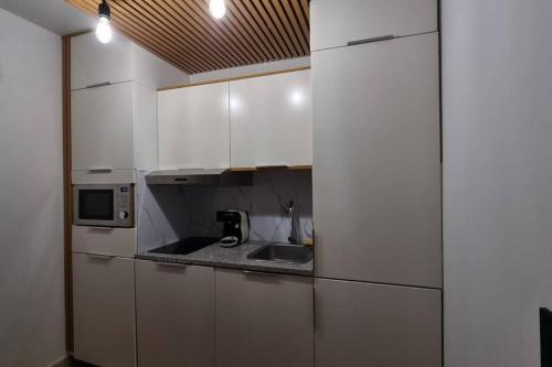 une cuisine avec des armoires blanches, un évier et un micro-ondes dans l'établissement Studio moderne St Germain les Corbeil - jacuzzi privatif, à Saint-Germain-lès-Corbeil