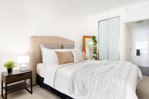 a white bedroom with a large bed with a night stand at A Cozy Studio CBD Next to Darling Harbour in Sydney