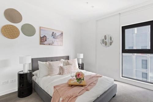 a white bedroom with a bed with a tray with flowers on it at An Amazing 2BR Apt with City Views in Southbank in Melbourne