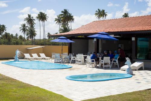 um pátio com uma piscina, mesas, cadeiras e guarda-sóis em Pousada Doutora Lindalva em Maragogi