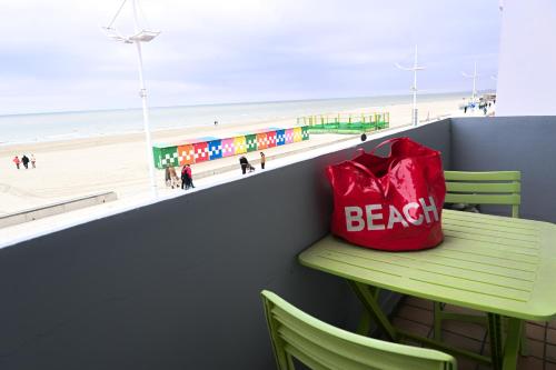 Chez Maïse - CR CONCIERGERIE في دونكيرك: وجود كيس احمر جالس على كرسي بجانب الشاطئ