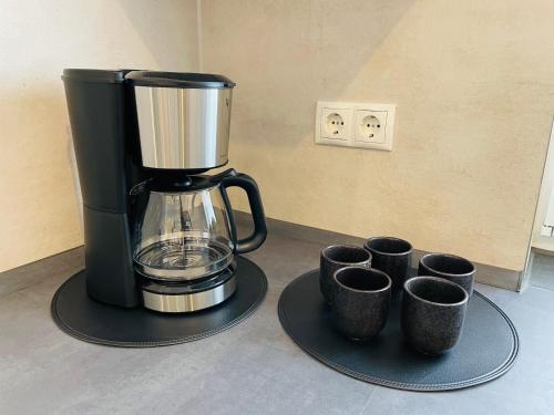 a coffee maker on a table with four cups at LIGHTPLACE - Moderne Apartments in Braunschweig - Balkon - Netflix - Am Kanal in Braunschweig