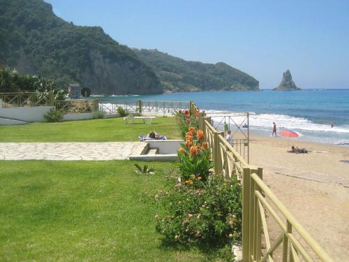 a fence next to a beach with people sitting on a bench at Beachfront 2-bed luxury Apartment - Agios Gordios Corfu Greece in Agios Gordios