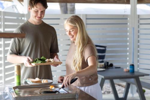 Ein Mann und eine Frau bereiten Essen auf einem Grill vor. in der Unterkunft Reflections Forster Beach - Holiday Park in Forster