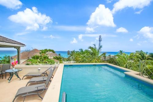 a swimming pool with chairs and a table and the ocean at Beacon Hill 304 by BSL Rentals in Saint Peter