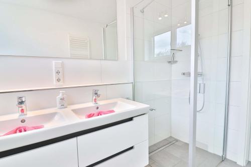 La salle de bains blanche est pourvue d'un lavabo et d'une douche. dans l'établissement Orange Hygge Haus, à Langeoog