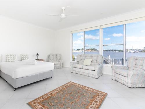 a white bedroom with a bed and two chairs at 21 Melaleuca Drive -LJHooker Yamba in Yamba