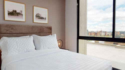 een slaapkamer met een wit bed en een raam bij Your Central Base near Unicentro in Bogota
