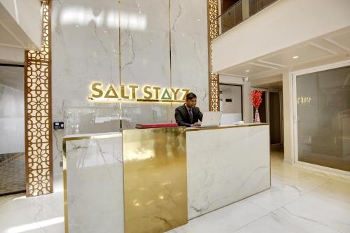 a man sitting at a counter in a lobby with a laptop at Saltstayz Premier - Near Golf Course Road & Sector 57 in Gurgaon