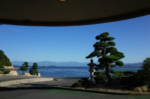 a tree and a statue in front of a body of water at Sennenmatsu in Imabari