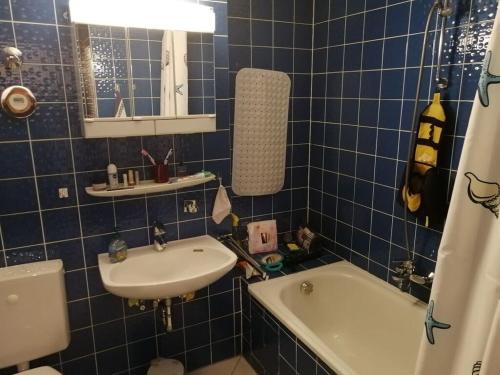 La salle de bains est pourvue de carrelage bleu, d'un lavabo et d'une baignoire. dans l'établissement Forest Residence Modern retreat, à Unterkirnach