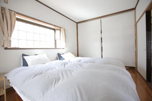 1 dormitorio con 2 camas con sábanas blancas y ventana en 一棟貸し別荘つる, en Matsue