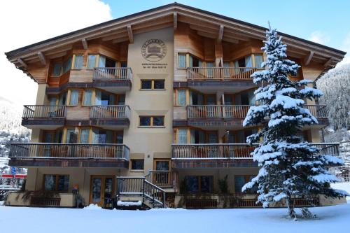 a large building in the snow with a snow covered tree at Hotel Garni Pegrà in Ponte di Legno