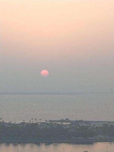 a sunset over the water with the sun in the sky at Cityscape Retreat Apartment in Sharjah