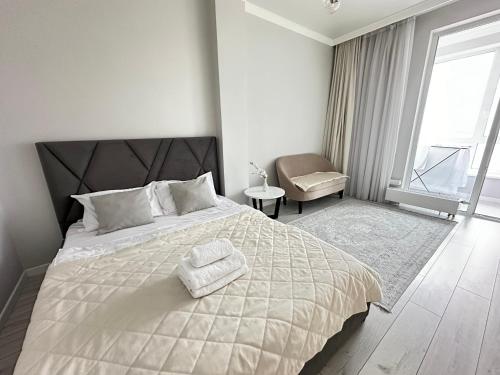 een slaapkamer met een wit bed met een stoel en een raam bij Esil Riverside Elite Apartments in Astana