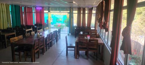 uma sala de jantar com mesas, cadeiras e janelas em Kandi Orchard Resort em Mussoorie