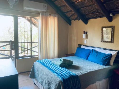 a bedroom with a bed with blue pillows and a window at Ivory Sands Safari Lodge in Marloth Park