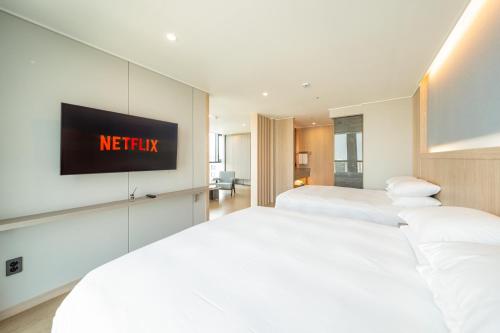 two beds in a hotel room with a tv on the wall at Jeju Bolton Hotel in Jeju