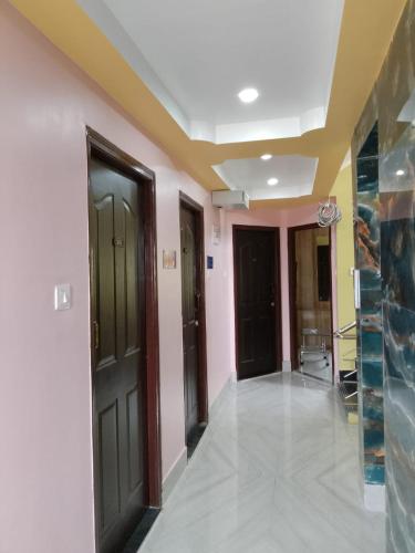 un couloir avec des portes noires et des murs roses dans l'établissement Hotel Red Velvet, à kolkata