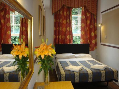 a bedroom with two beds and a mirror and flowers at Holland Court Hotel in London