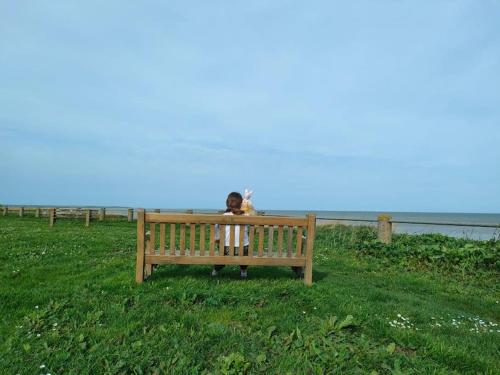 a person sitting on a bench near the ocean at Beachside Ground Floor Flat in Birchington