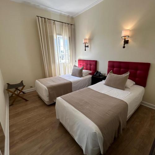 two beds in a hotel room with red headboards at Hotel Joao Padeiro in Aveiro