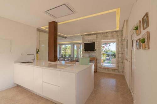 uma cozinha com armários brancos, um lavatório e uma televisão em Casa da Praia em Galé