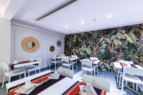 een restaurant met witte tafels en stoelen en een muurschildering bij Hôtel Princes de Catalogne in Collioure