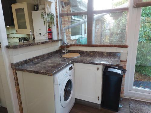 een keuken met een wastafel en een wasmachine bij The family room at the bungalow in Willesborough