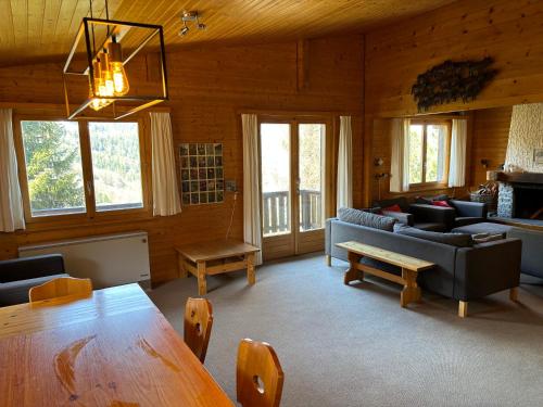 a living room with a table and couches and windows at Chalet Claire in Bürchen