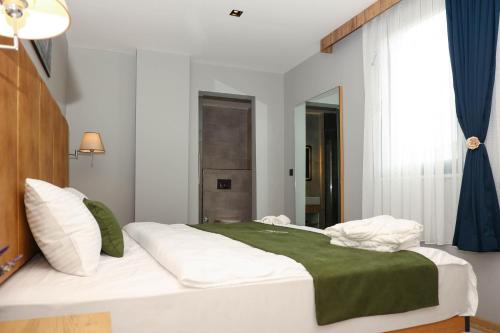 a bedroom with a white bed with a green blanket at Gardenmode Airport Hotel in Taşoluk