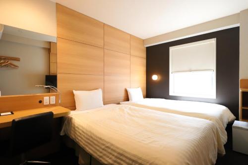 a bedroom with two beds and a desk and a window at Smile Hotel Kyoto Karasuma Gojo in Kyoto