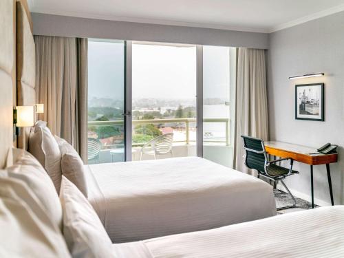 a hotel room with two beds and a desk at Novotel Sydney Brighton Beach in Sydney
