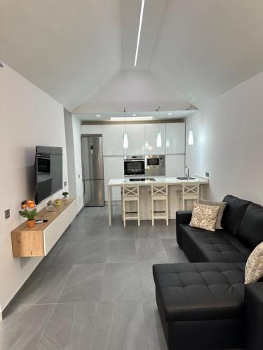 Una sala de estar con un sofá negro y una cocina. en Bungalow the Paradise, en Maspalomas