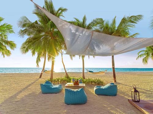 una playa con sillas, mesa y palmeras en One&Only Reethi Rah, en Reethi Rah