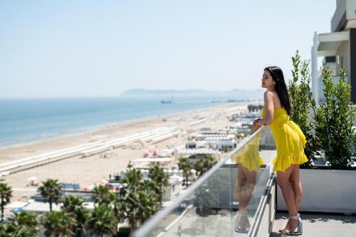 a woman in a yellow dress standing on a balcony overlooking the beach at Hotel Sporting Riccione in Riccione