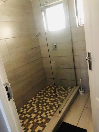 um chuveiro com uma porta de vidro e um piso xadrez em Elihle Guest house em Empangeni