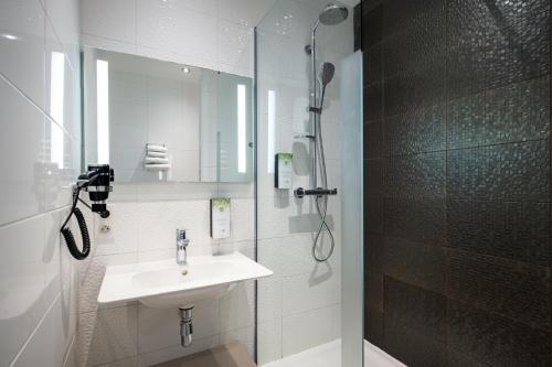 La salle de bains blanche est pourvue d'un lavabo et d'une douche. dans l'établissement Kyriad Prestige Saint-Malo, à Saint-Malo