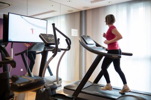 a woman running on a treadmill in a gym at Kyriad Prestige Saint-Malo in Saint Malo