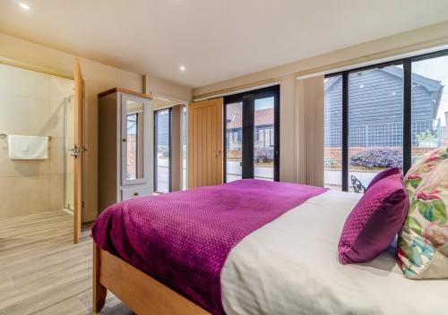 a bedroom with a large bed with purple sheets and windows at White House Lodges - Nightingale in Heveningham
