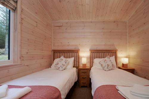 two beds in a room with wooden walls at Burgie Woodland Lodges in Forres