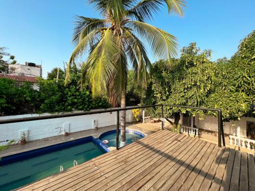 a deck with a palm tree and a swimming pool at Hermosa habitación en casa campestre con piscina cerca al aeropuerto in Santa Marta