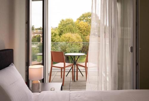 a bedroom with a bed and a balcony with a table and chairs at Lodges Hotel Morges in Morges