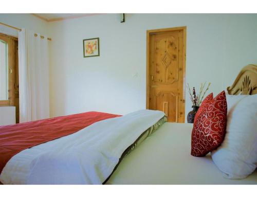 a bedroom with a bed with red and white pillows at Acharya Cottage, Manali in Manāli