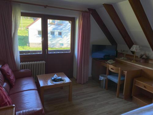ein Wohnzimmer mit einem Sofa, einem Schreibtisch und einem Fenster in der Unterkunft Hotel Faller in Breitnau