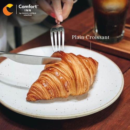 a person cutting a croissant on a plate with a fork at Comfort Inn, Udaipur in Udaipur