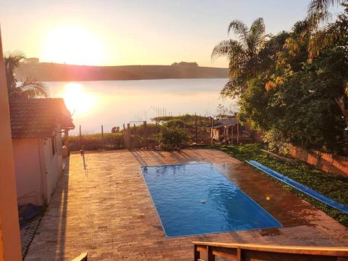 a swimming pool in front of a house with the sunset at Casa Alfenas Represa Furnas c/ Piscina Aquecida 12 pessoas in Alfenas