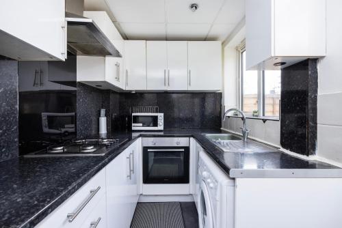 a kitchen with white cabinets and black counter tops at DAGENHAM 3 BEDROOMS2BATHS in Dagenham